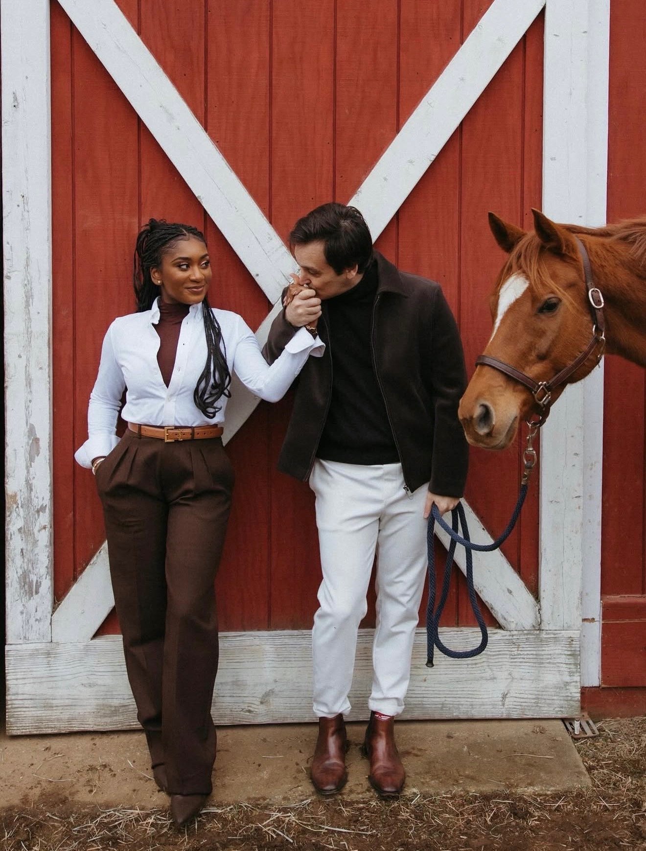 Marie and Matthew by a red barn door, with a chestnut horse beside them
